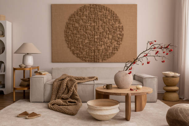 Interior design of living room interior with mock up poster, beige sofa, modern armchair, braided plaid, books, rowan in vase, pouf, lamp, bowl, rug and personal accessories. Home decor. Template.